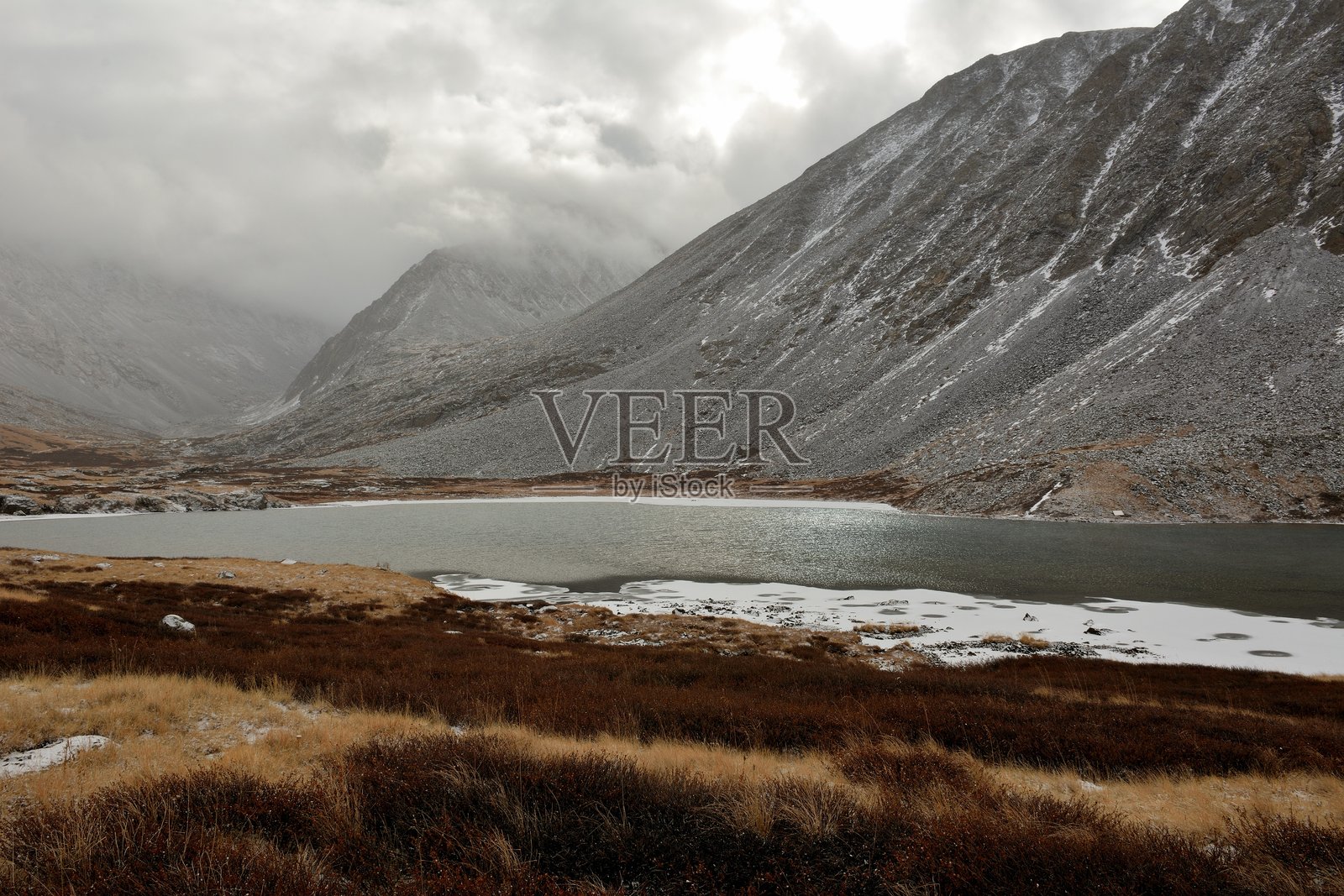 宽广湖泊的岸边，冰面上长满了红色苔藓，靠近高耸岩石的脚下，洒落着初雪。照片摄影图片