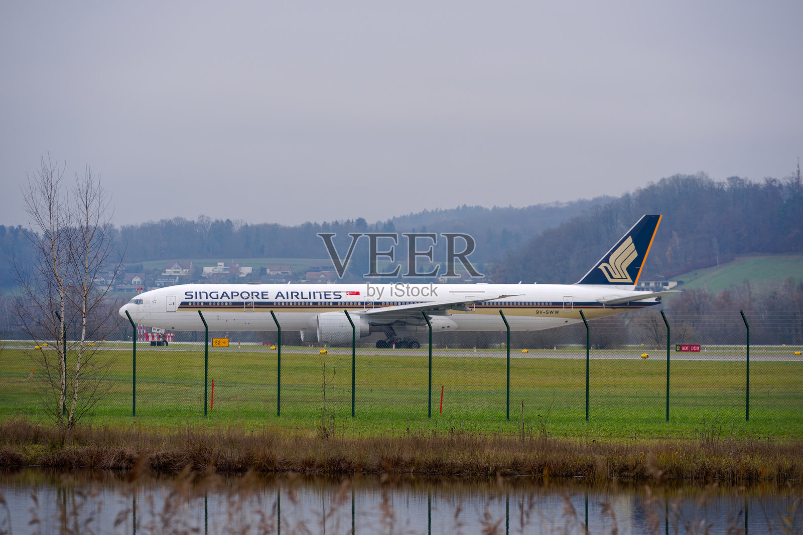 新加坡航空波音777-312ER客机侧视图，在瑞士苏黎世克洛滕机场的跑道上滑行，背景是雾蒙蒙的秋天。照片摄影图片
