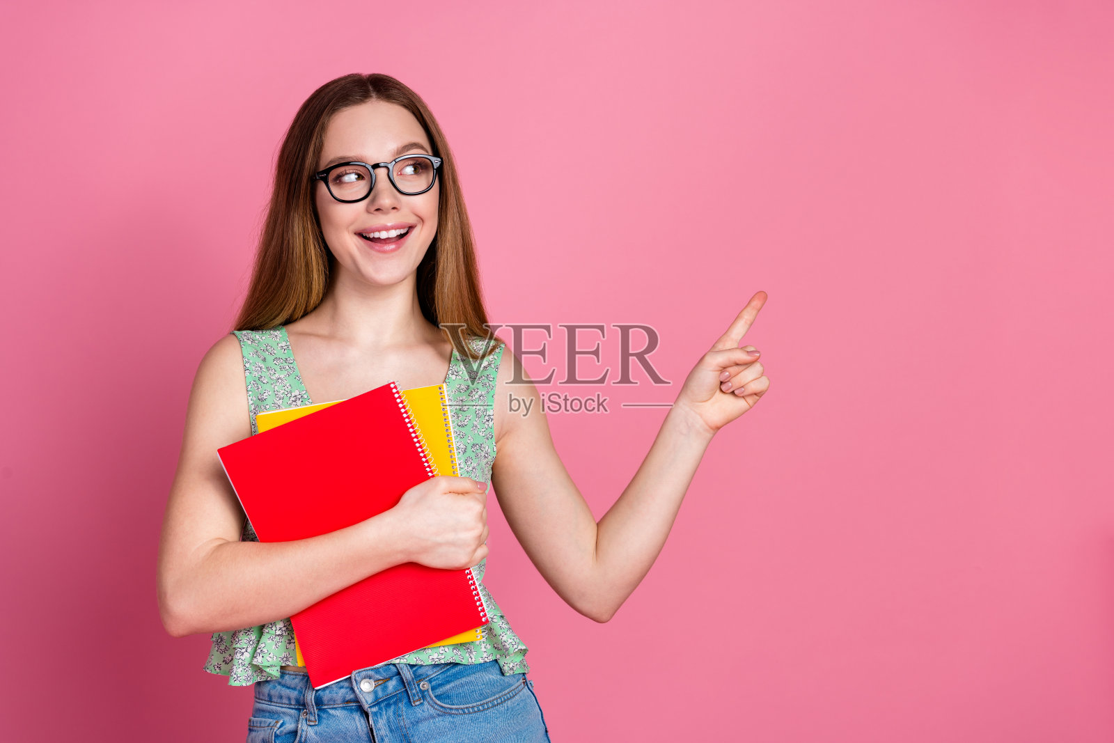 漂亮年轻女孩的肖像，手指指向空白处，穿着上衣，背景为粉色。照片摄影图片