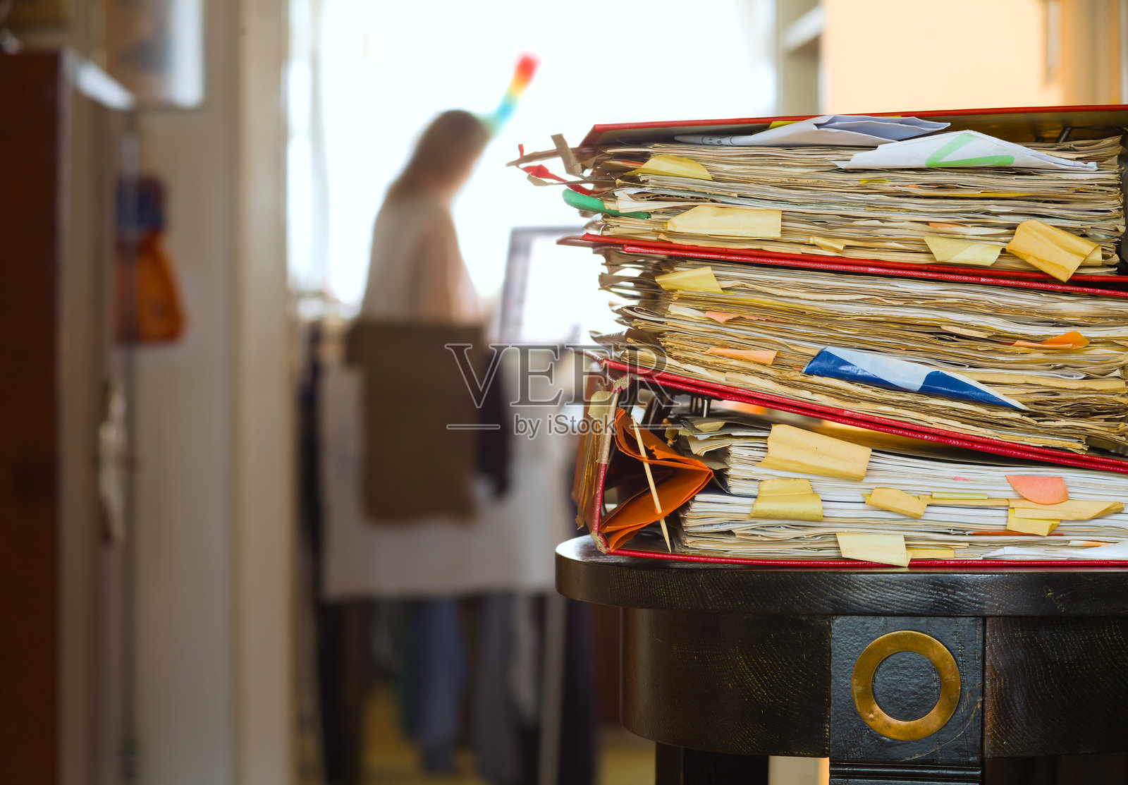 一堆文件夹和模糊的工作场所，无法辨认的女性与清洁工具。商业概念：家庭琐事与家庭办公室的双重负担，自由职业，居家工作，过度劳累，心理疲惫。照片摄影图片