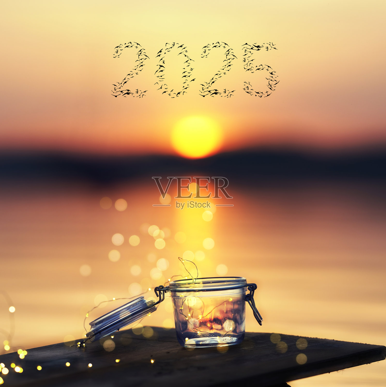 海滩上日落时分，打开的玻璃杯中闪烁的灯光，鸟儿飞翔成2025的形状，象征着新年的开始。照片摄影图片