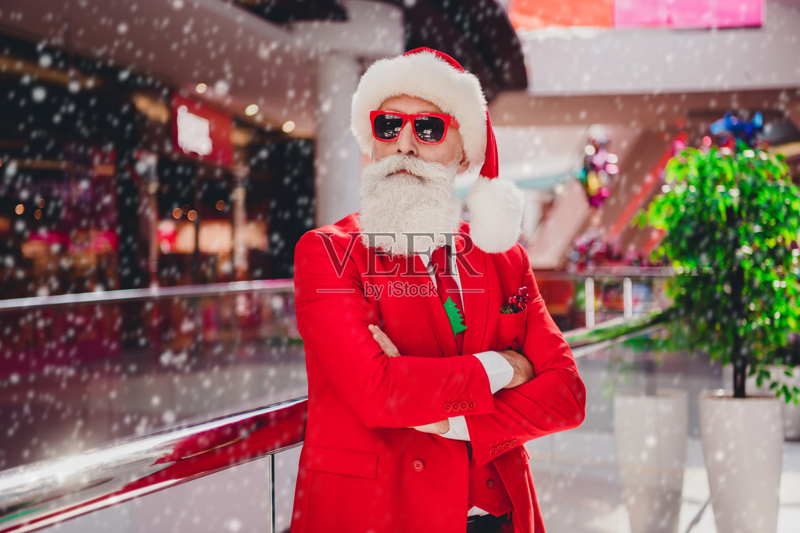 自信酷炫的圣诞老人戴着墨镜，双臂交叉，在购物中心的商店内走动。照片摄影图片
