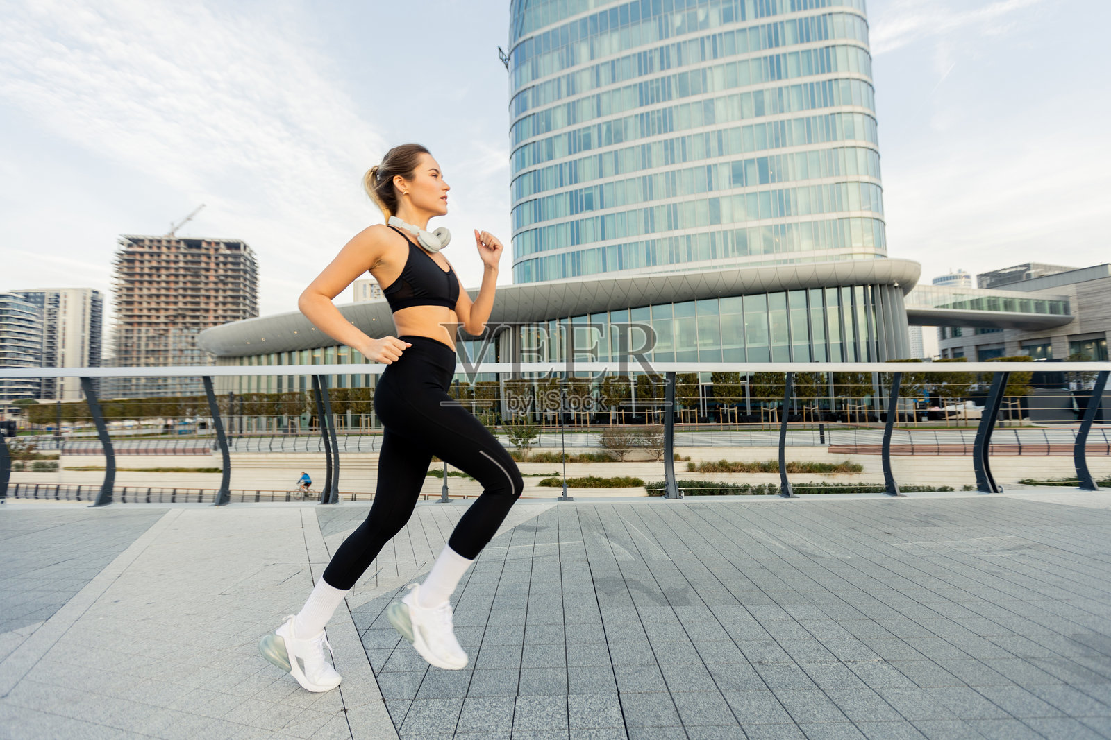 一位坚定的女性在现代城市环境中自信地慢跑，展示她的健身之旅，背景是流线型的建筑。照片摄影图片