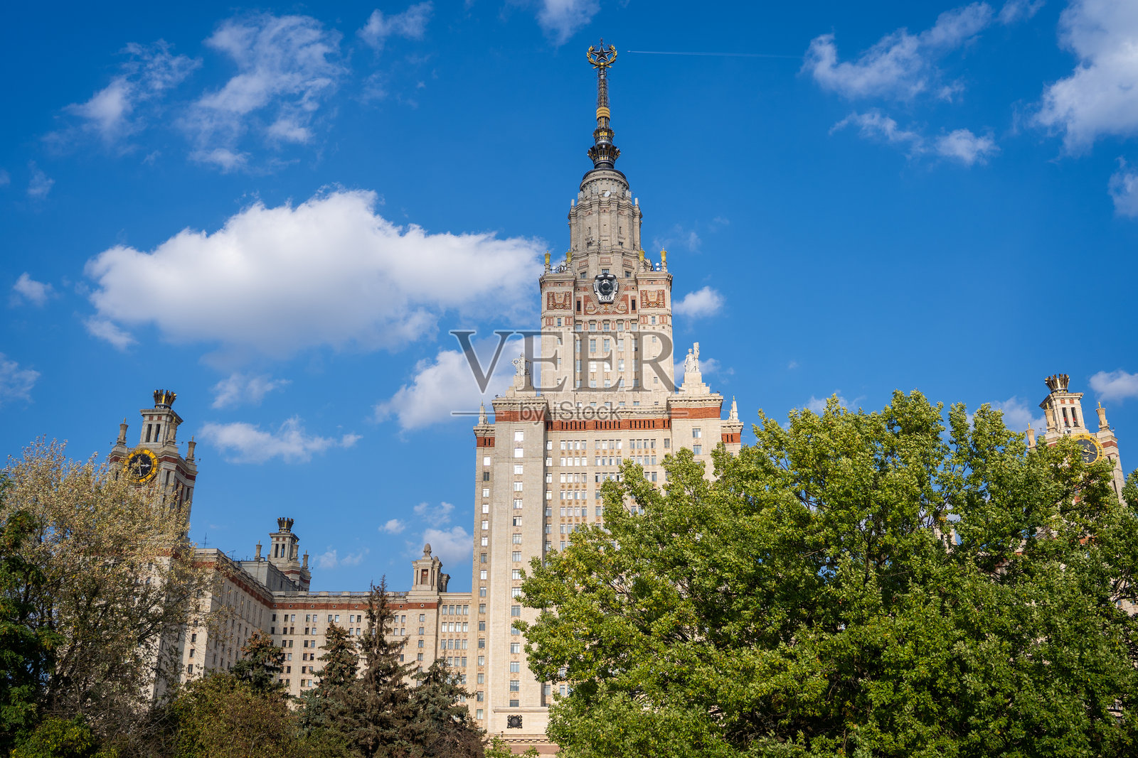 莫斯科，俄罗斯 - 2023年9月30日：夏日里透过公园树木看到的莫斯科国立大学大楼。照片摄影图片