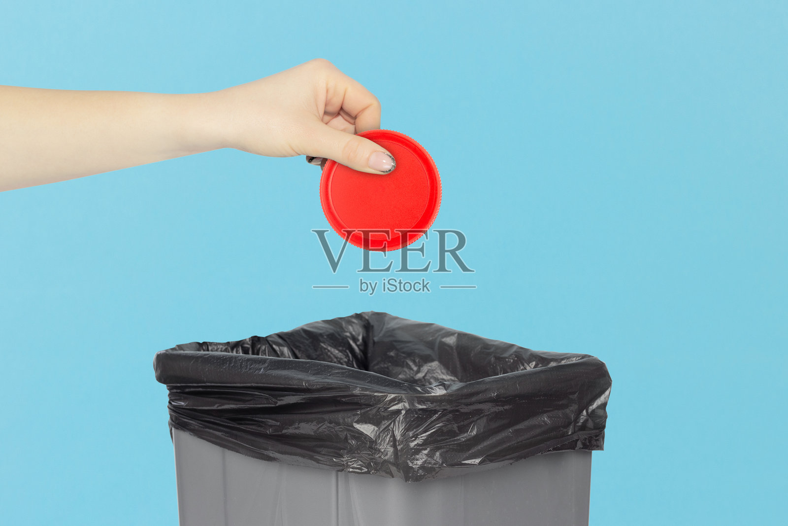 将塑料瓶的瓶盖扔进垃圾桶，手中拿着塑料瓶的瓶盖，站在垃圾桶前，塑料回收概念照片摄影图片
