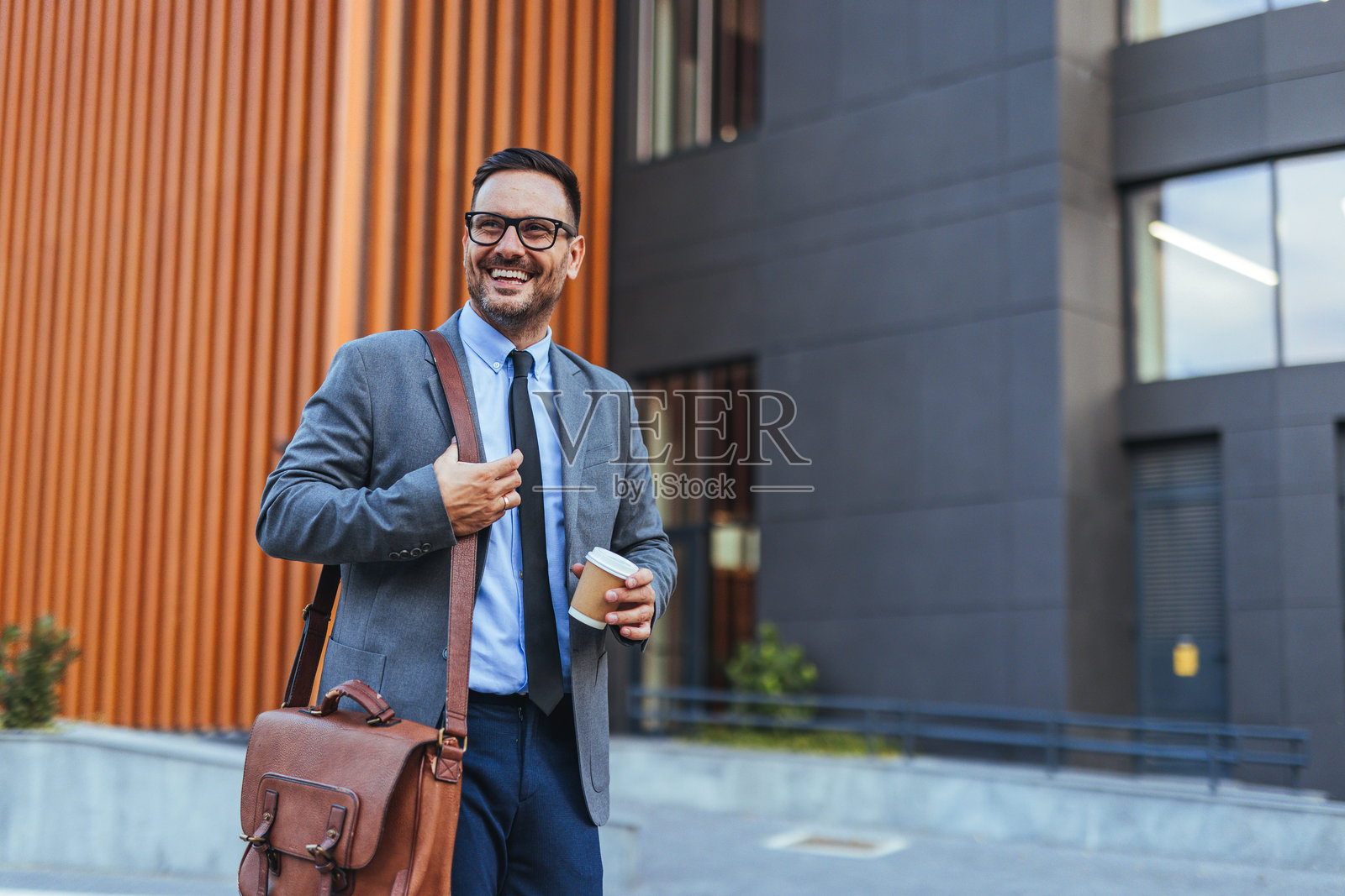 自信的商人在办公大楼外走着，手里拿着咖啡照片摄影图片