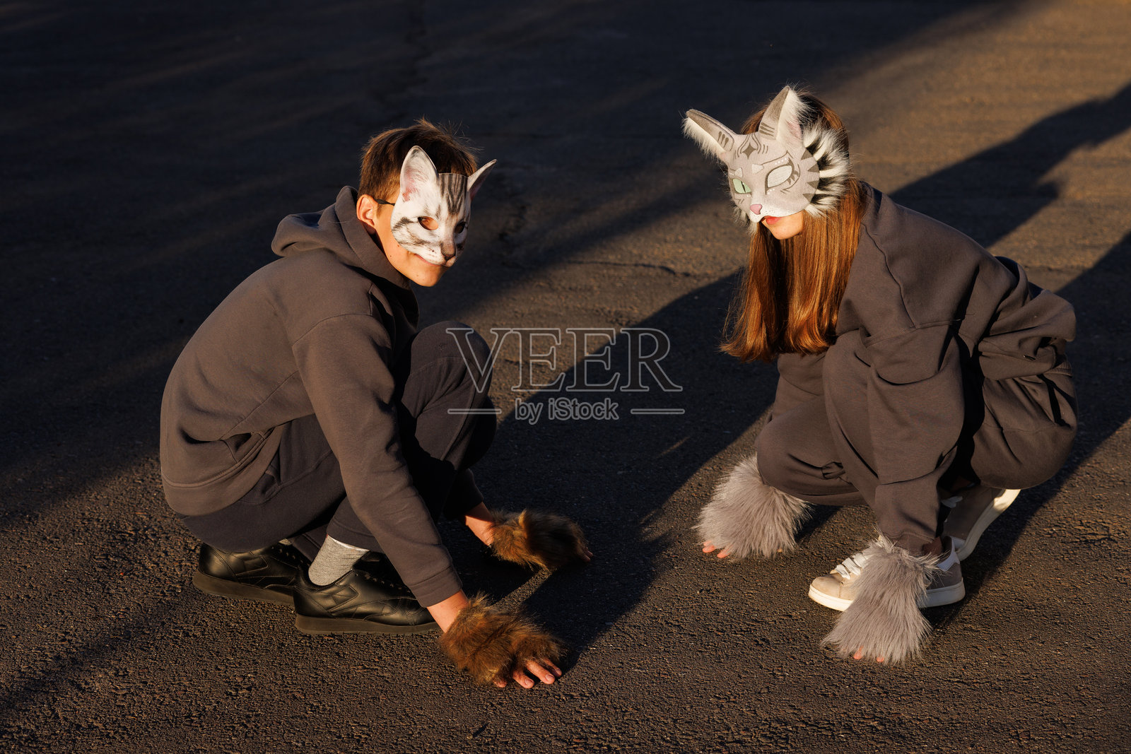 戴着猫面具的女孩和男孩在城市中进行四足运动，动物行为模拟，四足运动体育。照片摄影图片