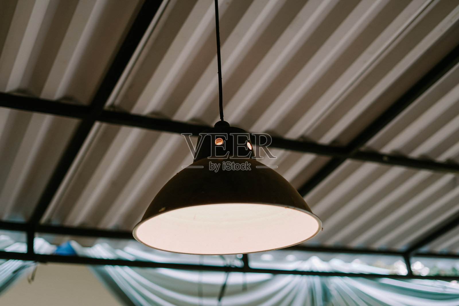 黑色工业风吊灯悬挂在波纹金属天花板上。照片摄影图片