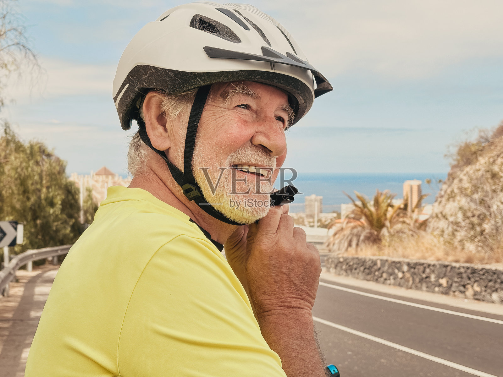 快乐微笑的活跃胡须老年男子在骑自行车前调整头盔，街道上骑行。老年男性享受健康的生活方式和退休或假期。照片摄影图片
