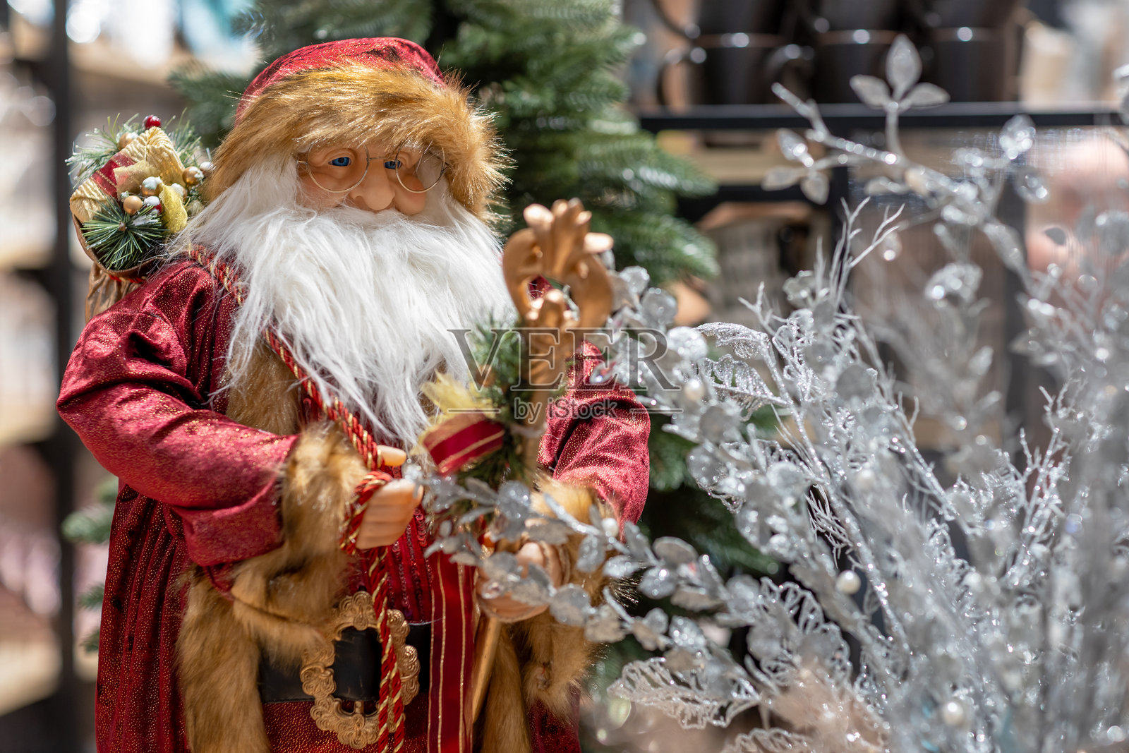 圣诞老人玩偶站在商店货架上，背景是圣诞树。留白区域可供添加文字。照片摄影图片