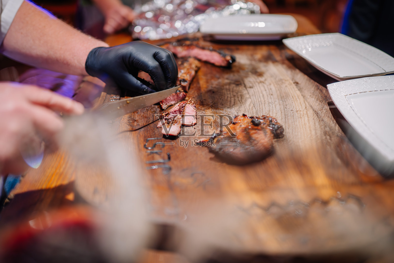 一位厨师在木板上切割烤牛排，准备盛放在白色盘子上。牛排外焦里嫩，木板上的雕刻细节清晰可见。照片摄影图片