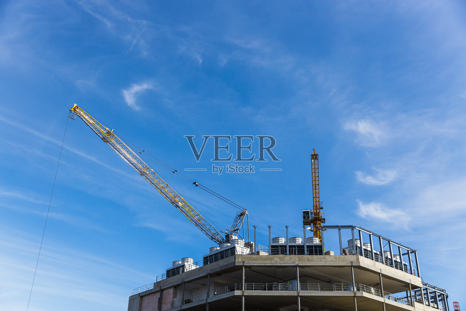 建筑工地上，起重机在钢筋混凝土建筑顶部上方作业照片摄影图片