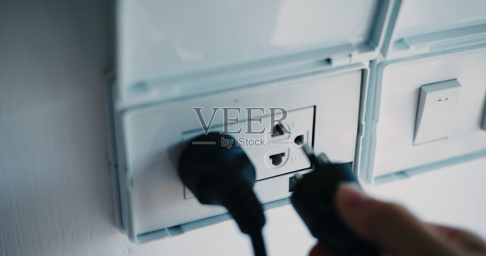 手部特写插入电源插座的电插头。照片摄影图片