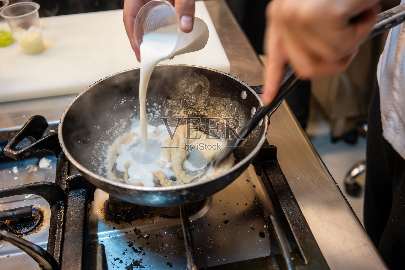男性厨师在厨房炉灶上用炒锅烹饪食物，静态准备中。照片摄影图片