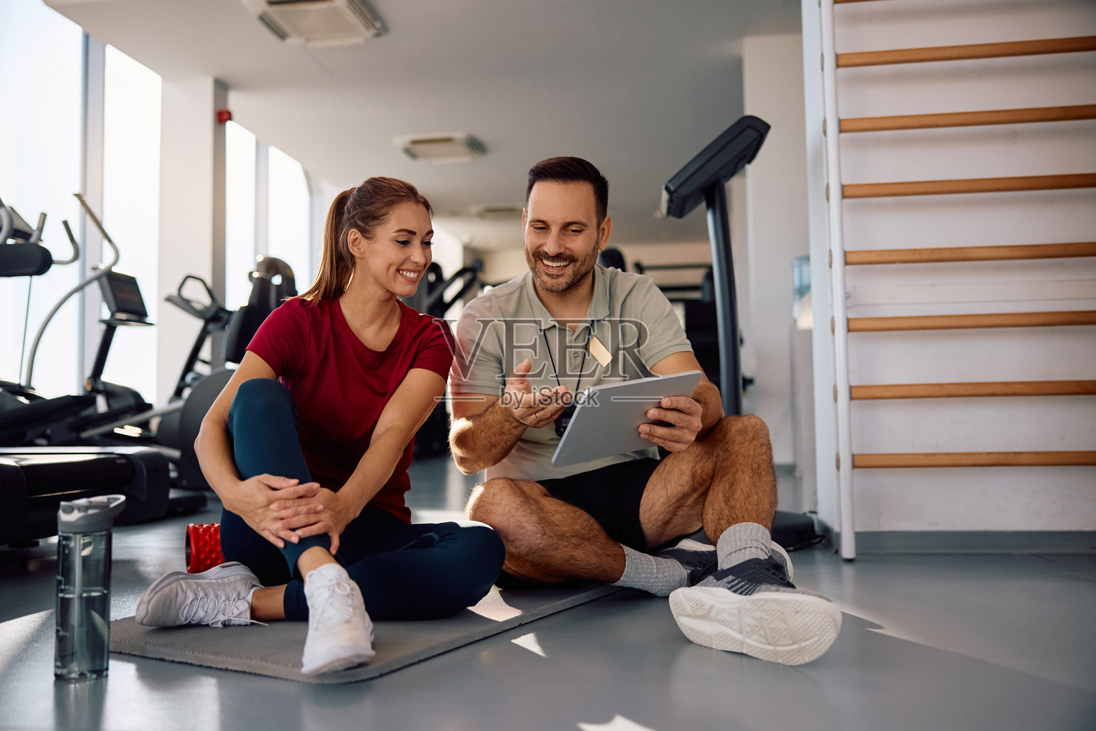 快乐的女运动员和她的私人教练在健身房用触控板计划锻炼课程。照片摄影图片