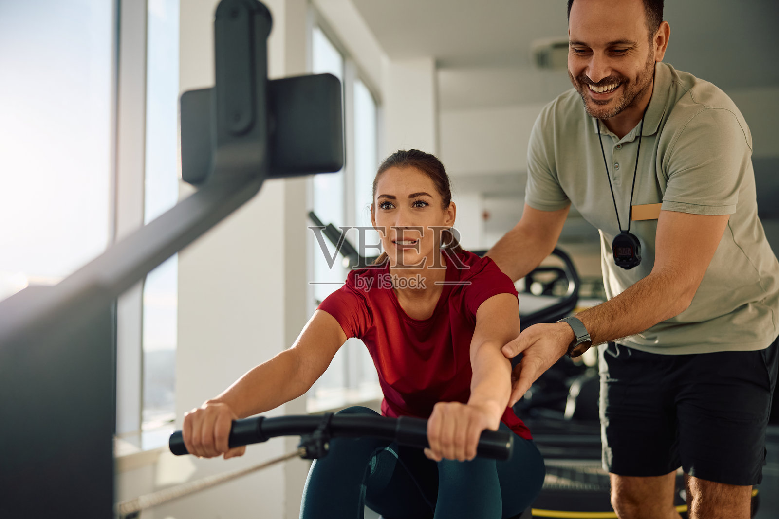 在健身房里，一位运动女性在私人教练的指导下使用划船机锻炼。照片摄影图片