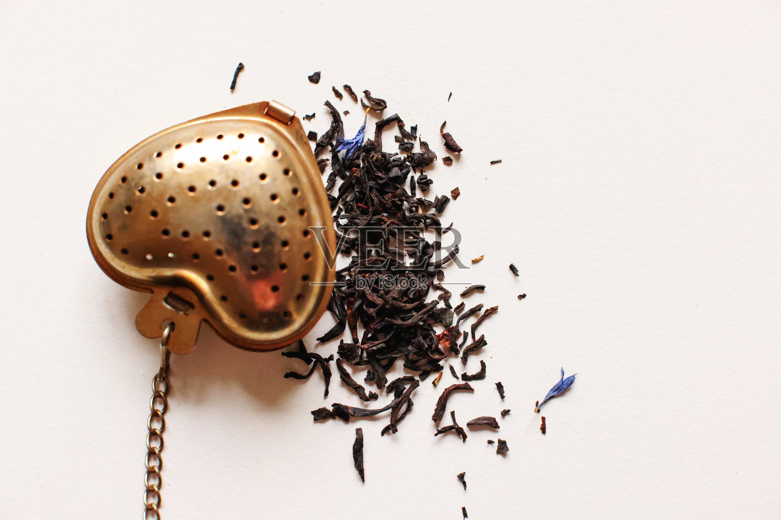 不锈钢茶包内的茶叶，周围散落着一些茶叶，背景为白色。照片摄影图片