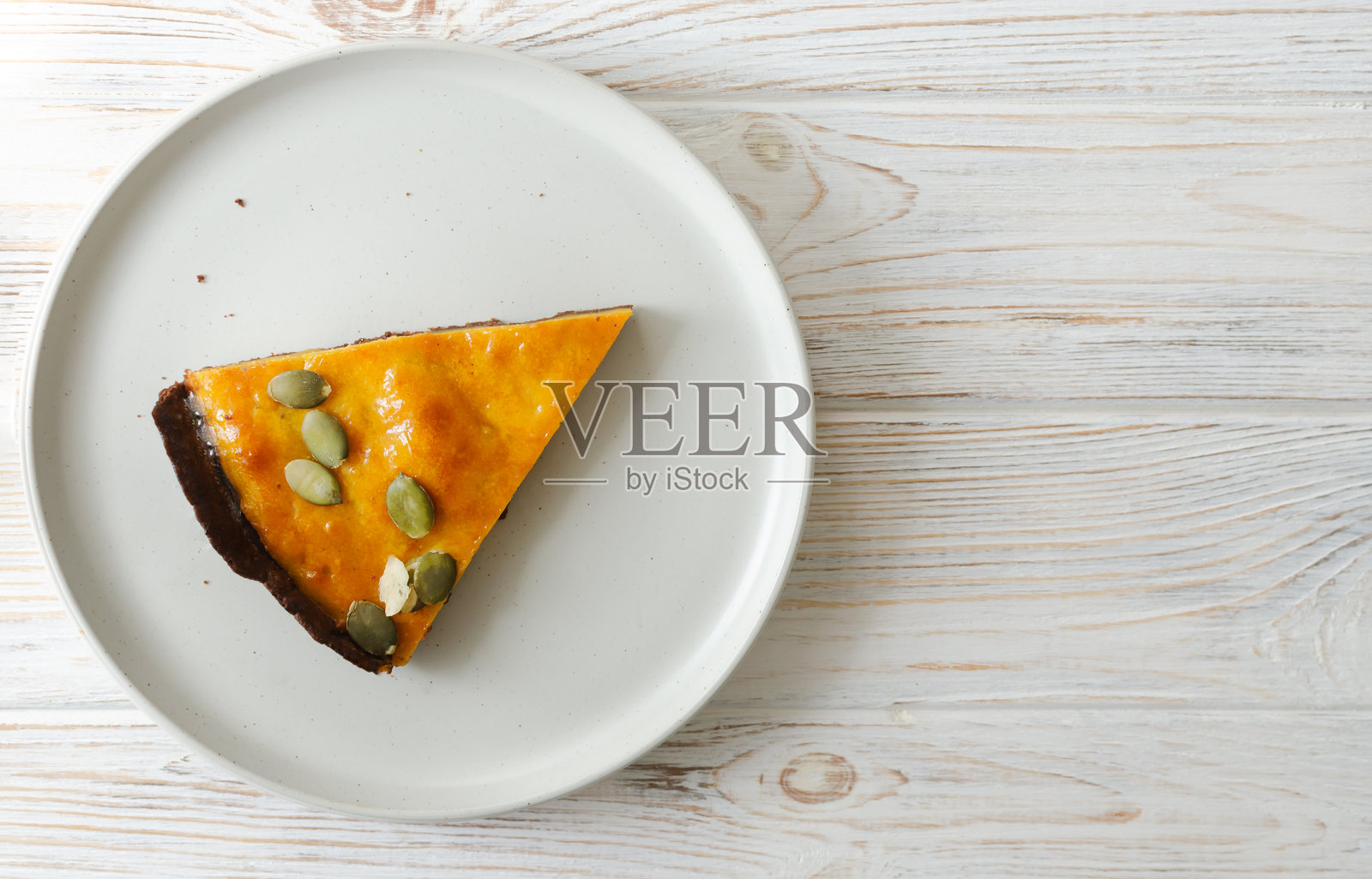 一块橙色南瓜派，上面撒有干种子，放在桌子上的白色盘子里。秋天的氛围。茶点时光的概念。横向构图。俯视图。留白空间。照片摄影图片