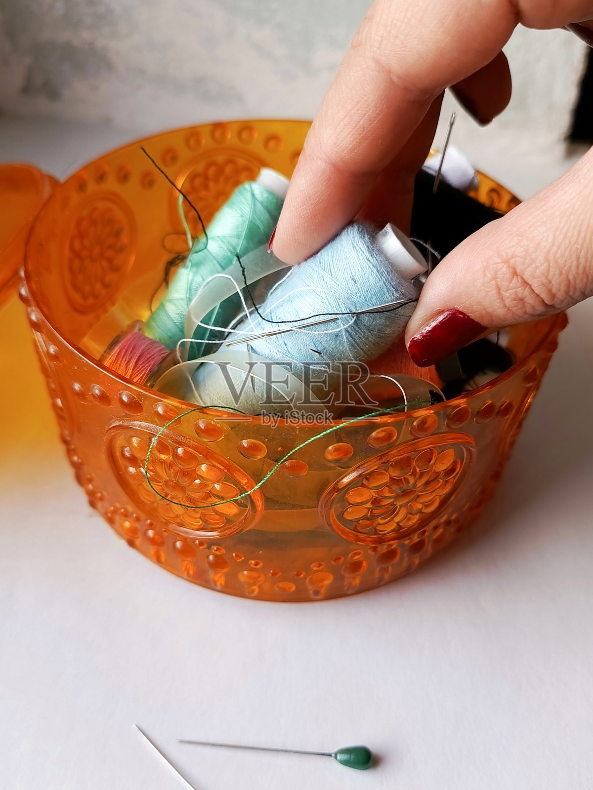 一只女性的手从装有线和针的盒子中取出一卷蓝色线。缝纫和衣物修补的概念。背景，留有文字空间。照片摄影图片