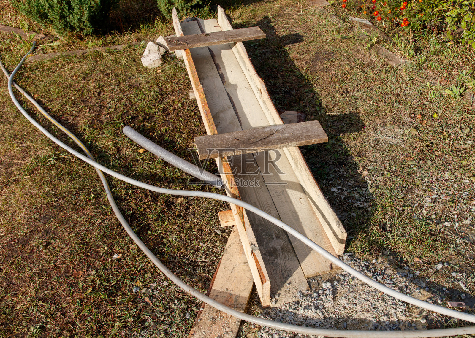 一块木板放在地上，旁边有一条灰色的水管。照片摄影图片