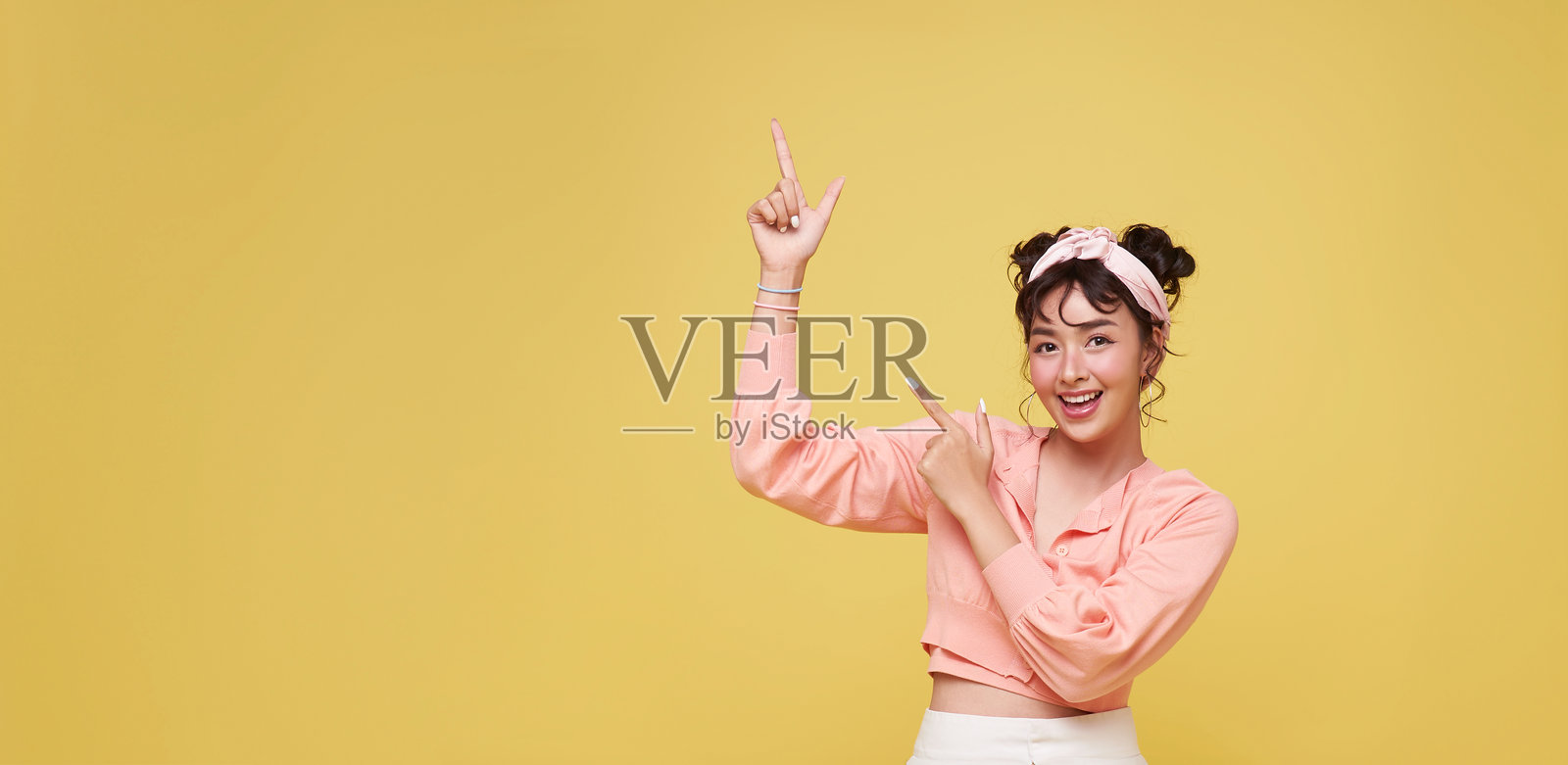快乐的年轻亚洲少女站在黄色背景前，手指指向前方。照片摄影图片