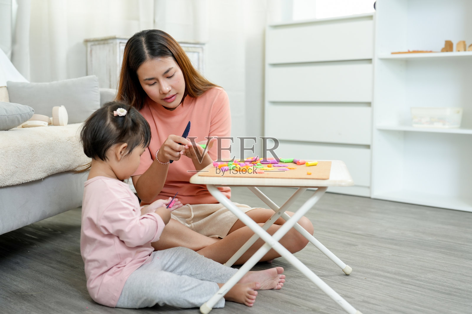 亚洲母亲在舒适的家中环境中帮助年轻女儿制作五彩的橡皮泥，强调早期儿童教育、关爱和家庭亲密关系。照片摄影图片
