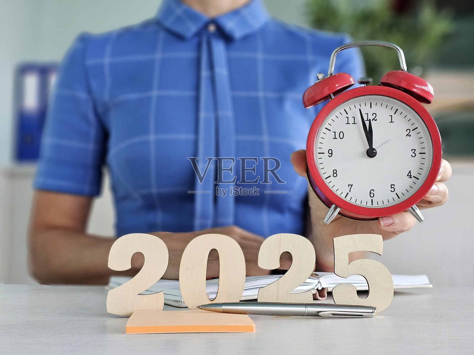 女人手持一个红色闹钟，旁边是一个木制数字，表示年份2025。照片摄影图片
