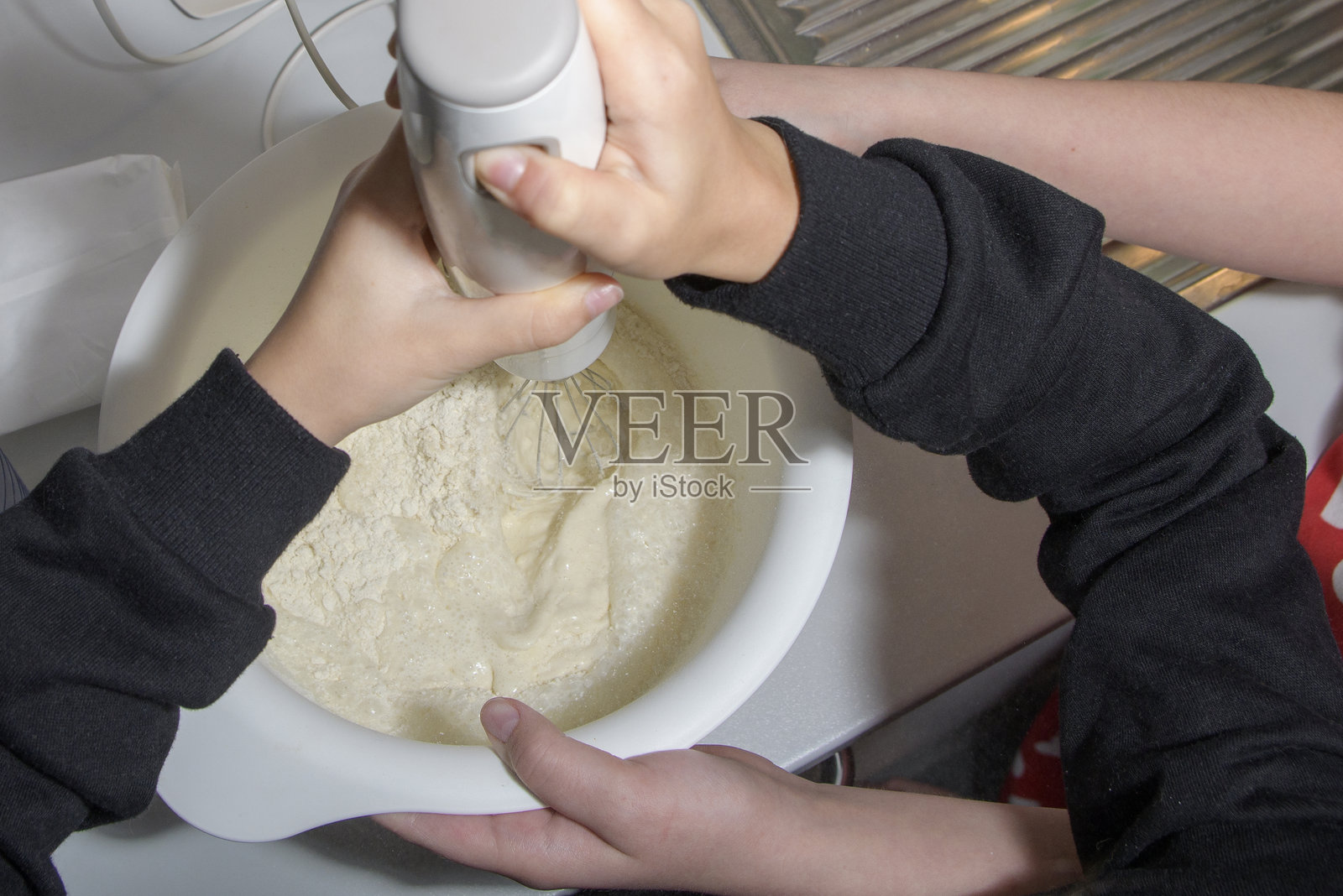 一个女孩在准备面团时拿着搅拌器，另一个女孩则帮忙托着碗。照片摄影图片