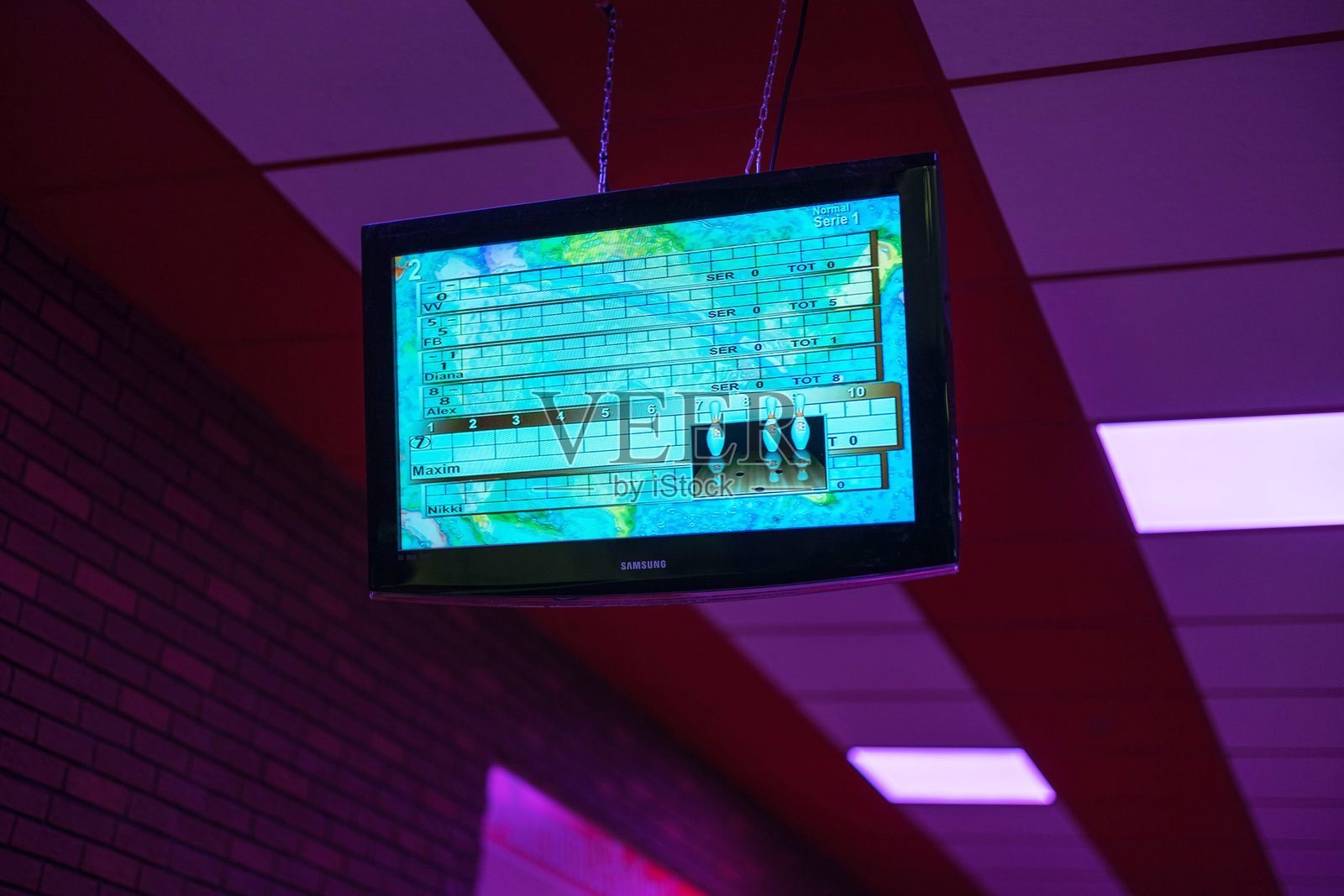 在霓虹灯闪烁的保龄球馆中，屏幕上显示着球员的名字和分数的保龄球记分板。照片摄影图片