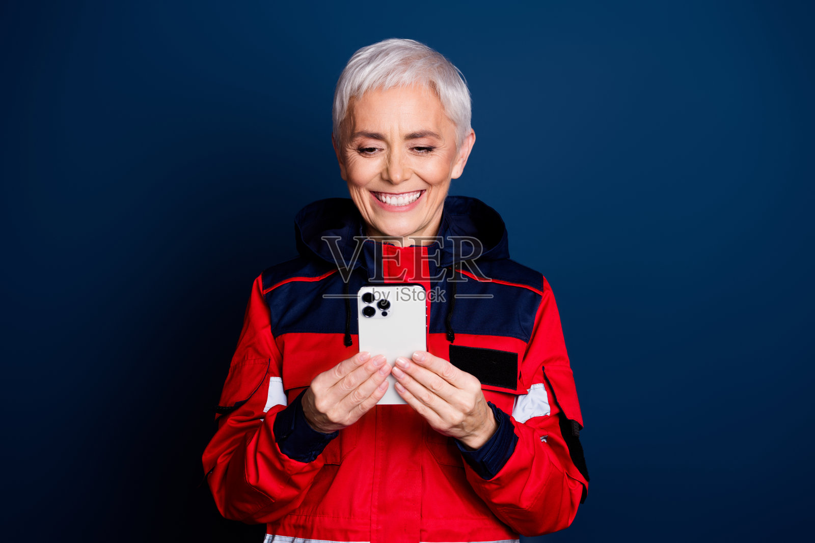 可爱的退休女士在深蓝色背景下穿着红色制服，提供紧急医疗帮助，手持设备。照片摄影图片