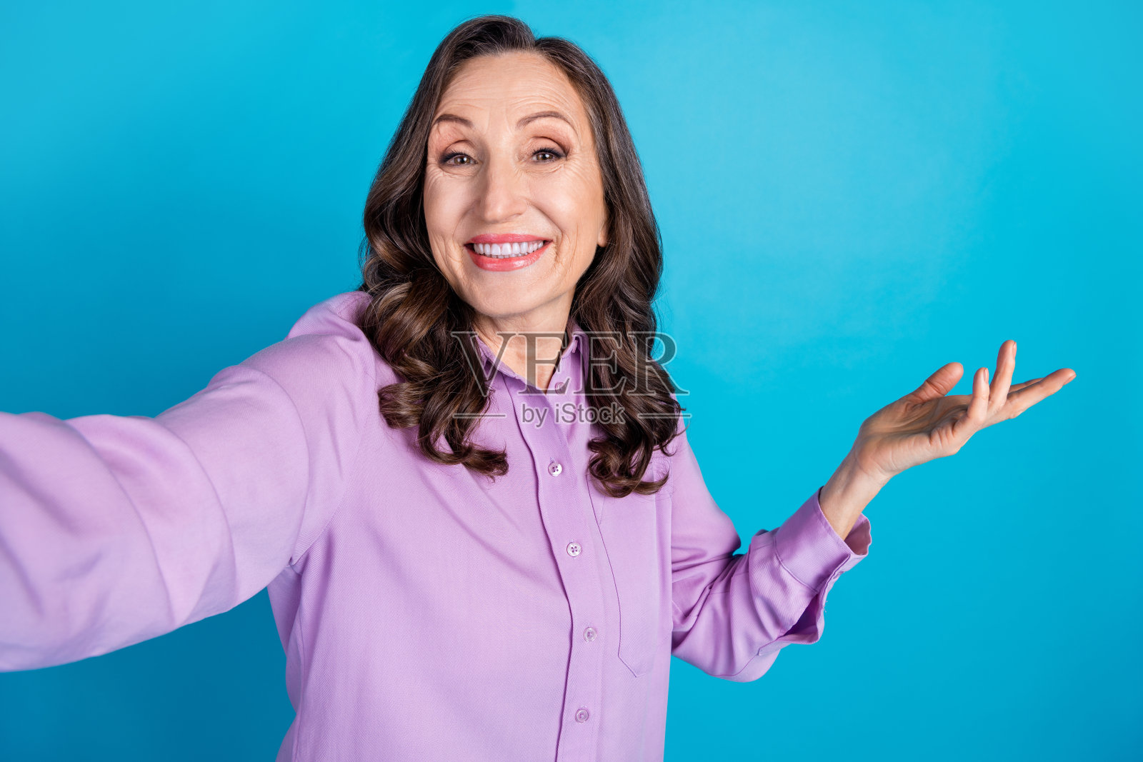 一位穿着紫色上衣的迷人女士在蓝色背景下自拍，展示出空荡荡的手臂。照片摄影图片