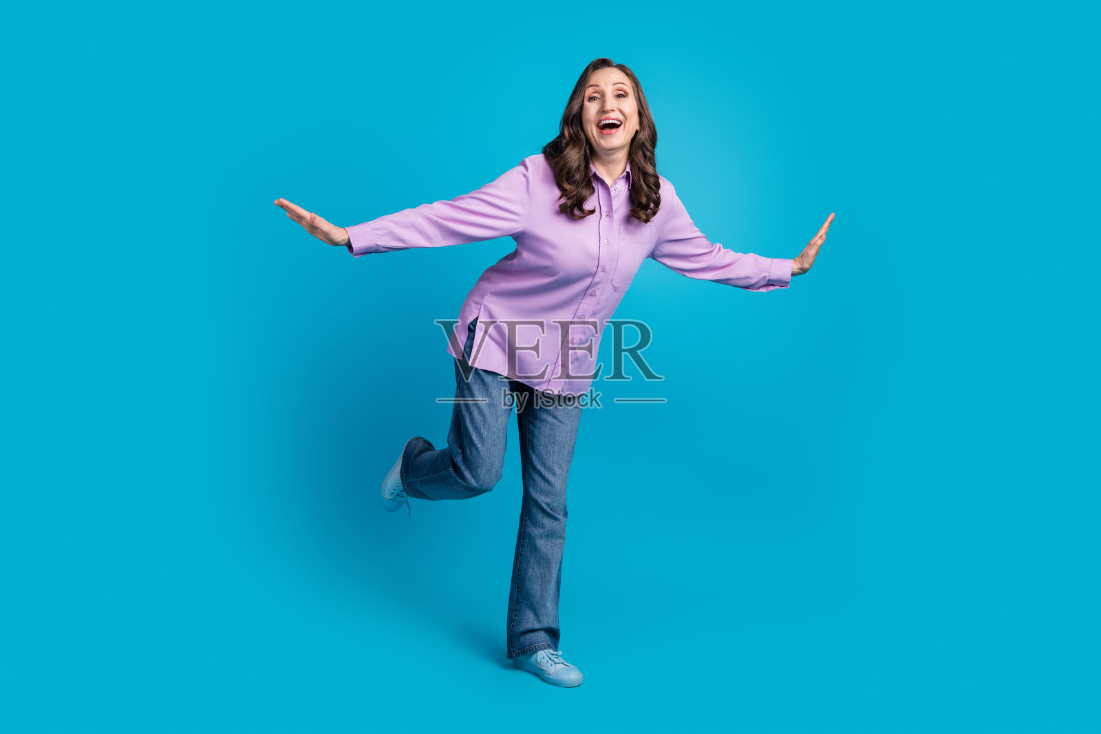 穿着紫色上衣的快乐漂亮女士全身照，享受乐趣，背景为空旷的蓝色。照片摄影图片