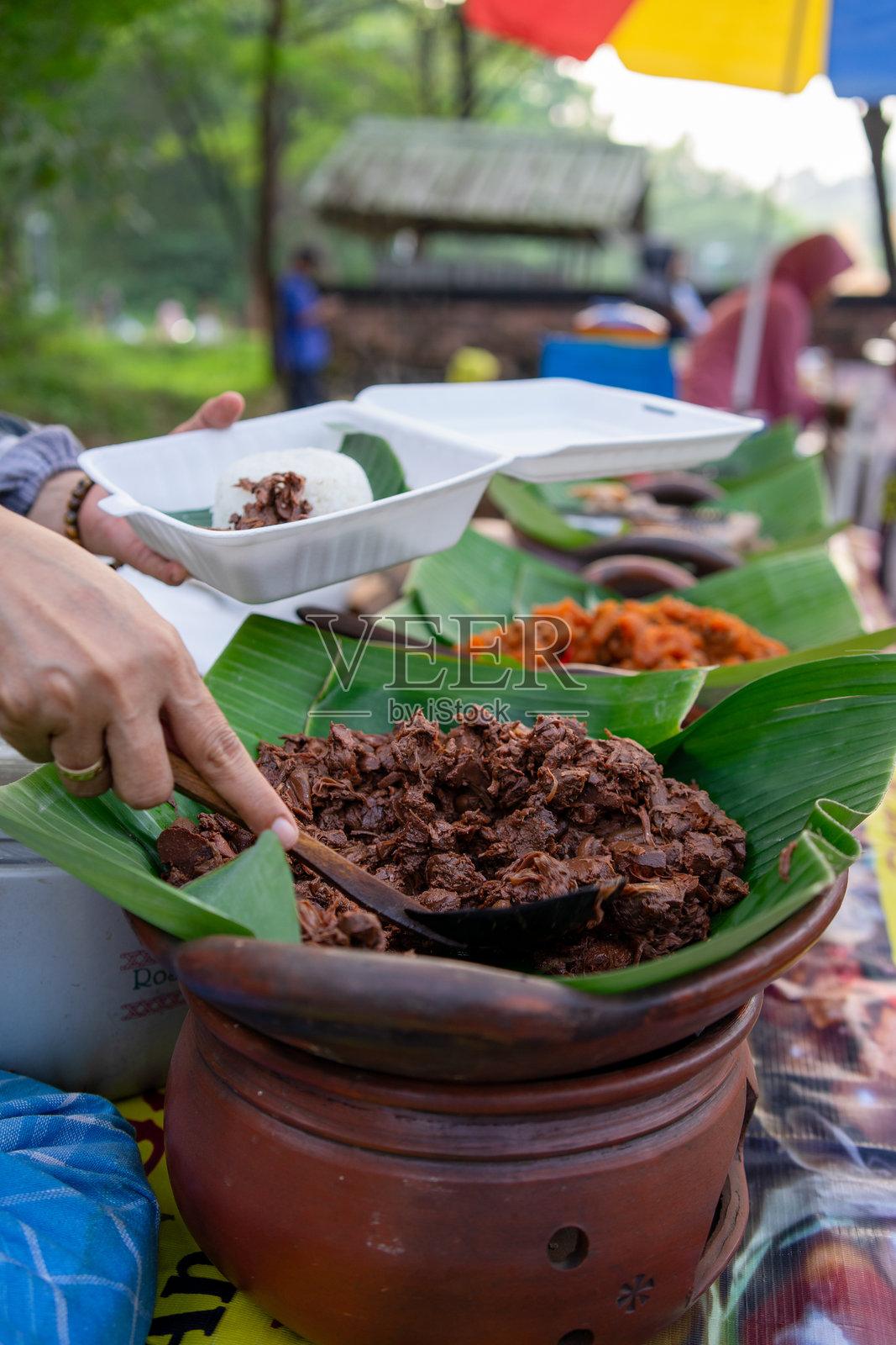 卖家正在用木勺挑选Gudeg蔬菜。照片摄影图片