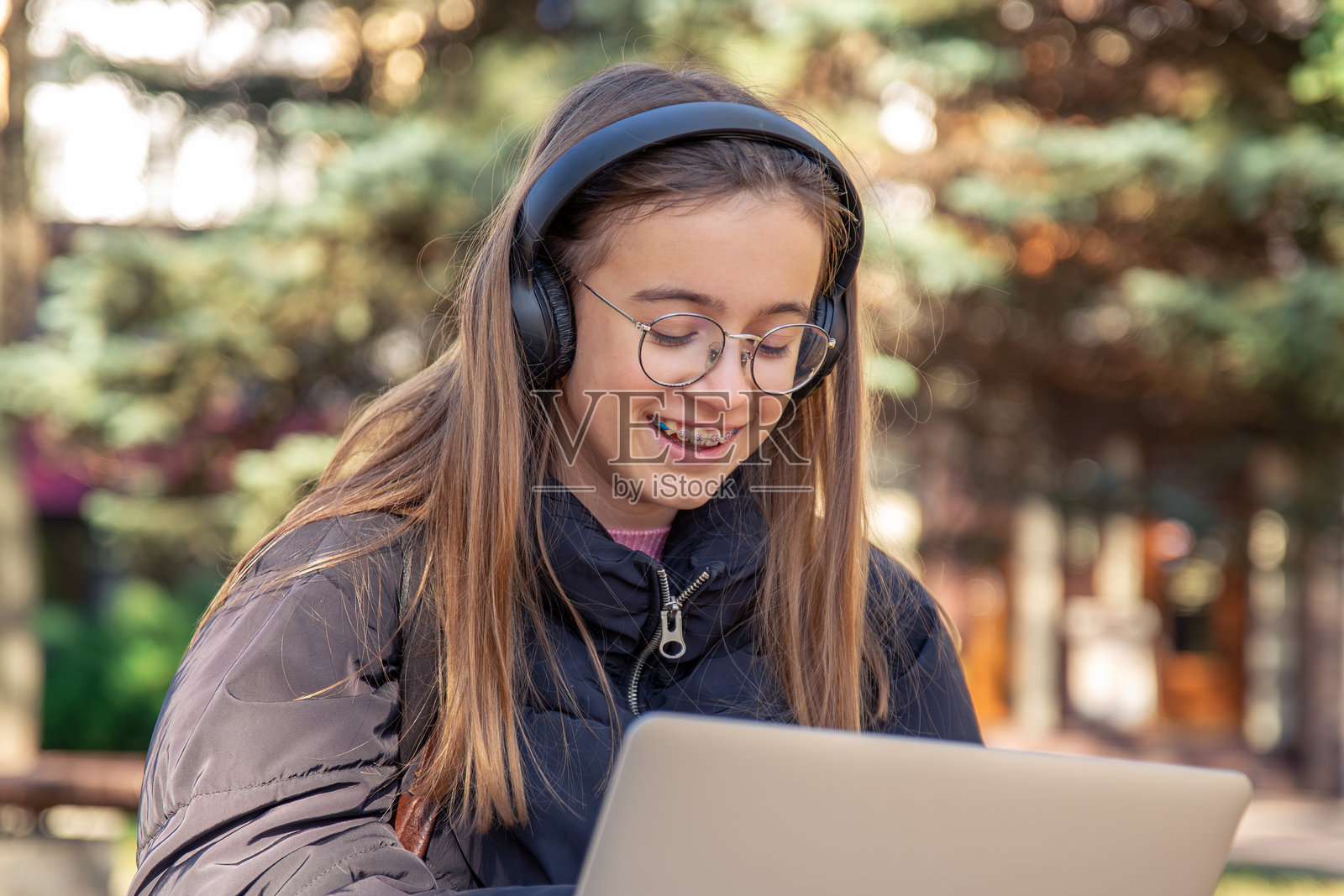 快乐的少女戴着耳机在笔记本电脑上工作。情感概念。照片摄影图片