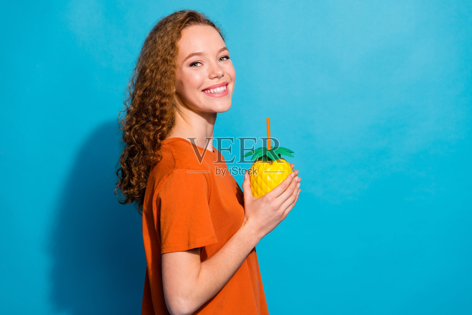 积极的女孩手持菠萝杯，背景为蓝色。照片摄影图片