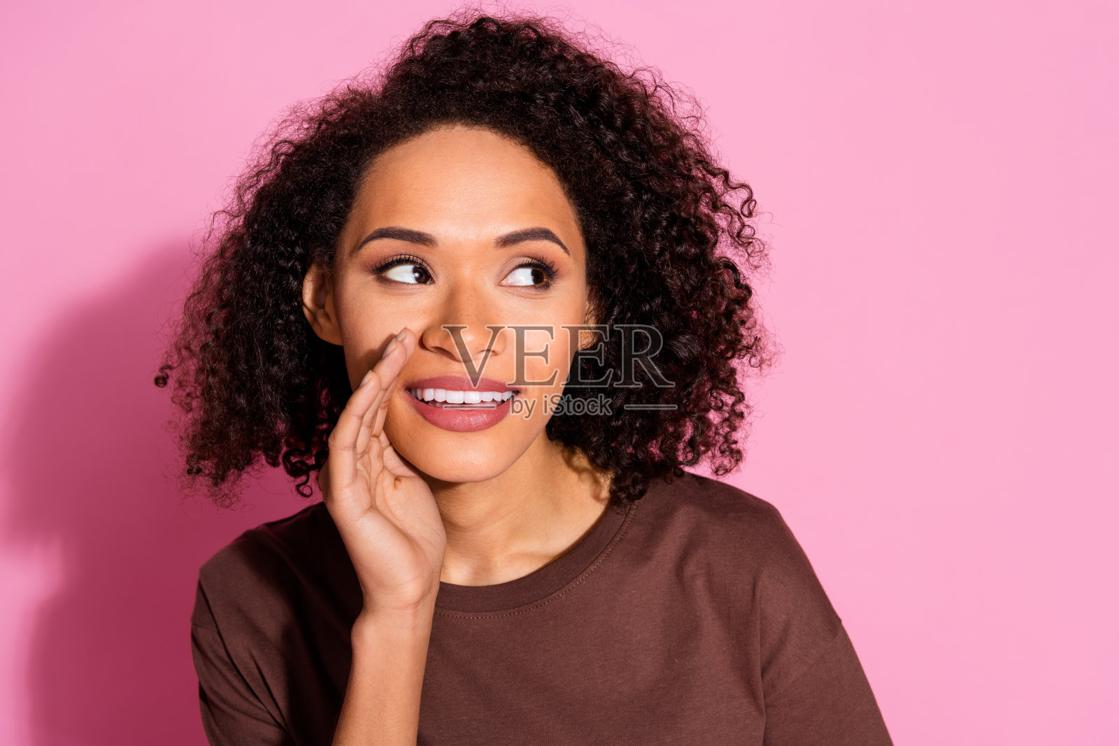 穿着棕色T恤的漂亮年轻女士在粉色背景前与空旷空间对话的肖像照片摄影图片