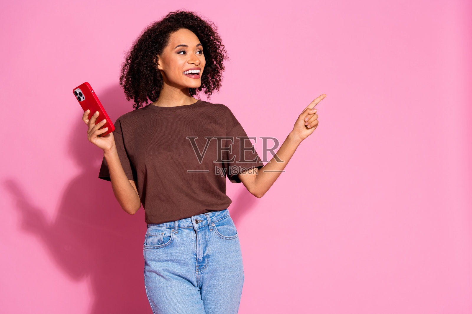 迷人可爱的女孩穿着棕色时尚服装，微笑着看向粉色背景上的空白空间。照片摄影图片