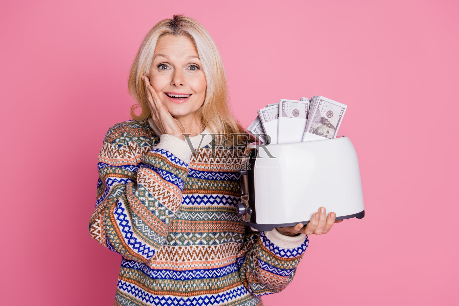穿着毛衣的可爱老年女性与烤面包机和钞票的肖像，背景为粉色。照片摄影图片