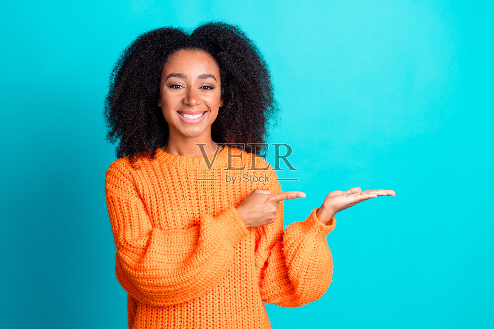 可爱的年轻女士在水绿色背景下穿着时尚的橙色针织服装，指向并保持空白空间的照片肖像。照片摄影图片