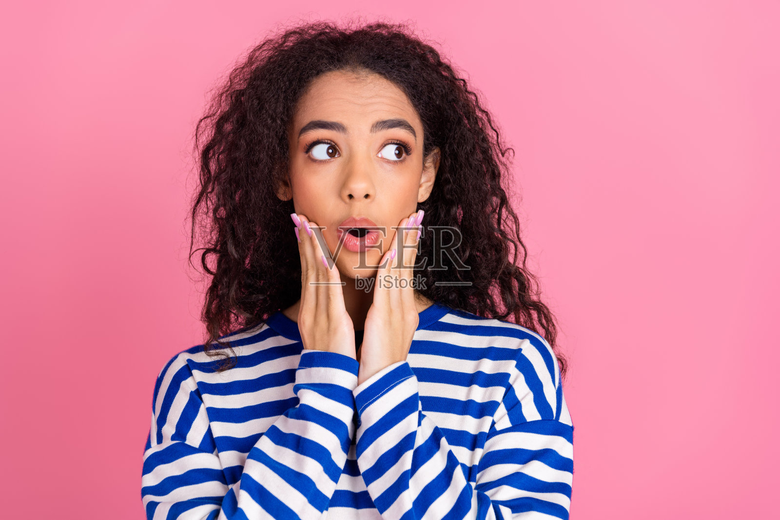 穿着条纹毛衣的漂亮年轻女孩凝视空旷的空间，背景为粉色。照片摄影图片