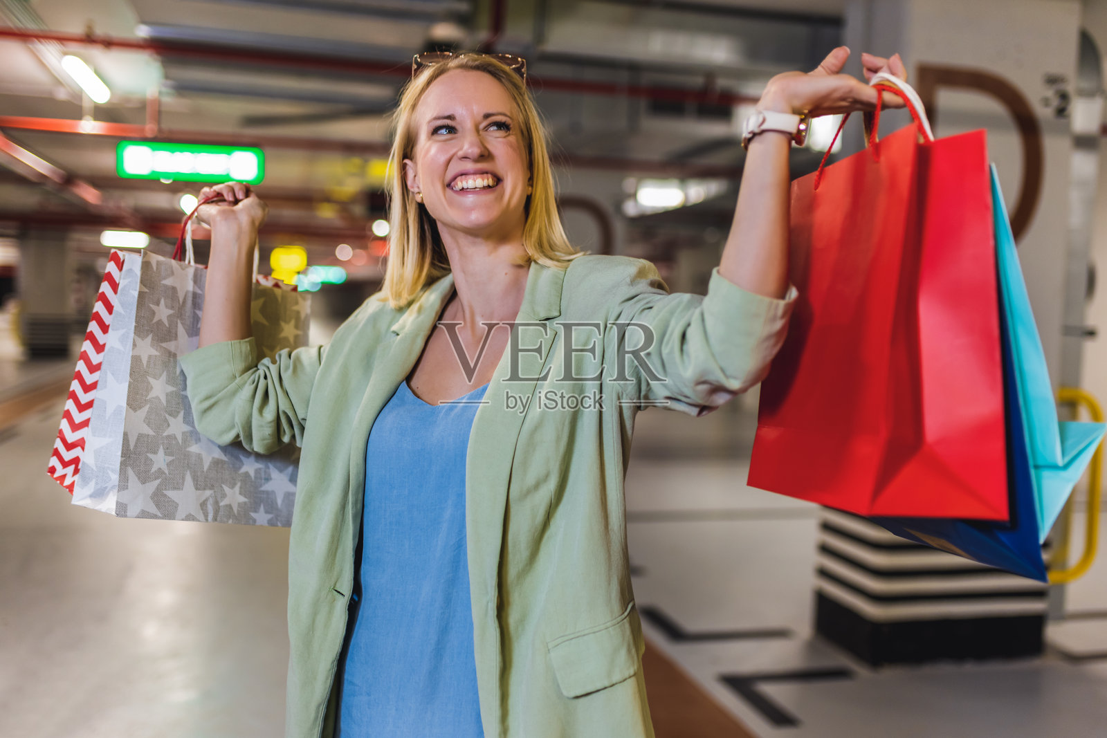金发女性提着购物袋在地下车库里走动的肖像。照片摄影图片