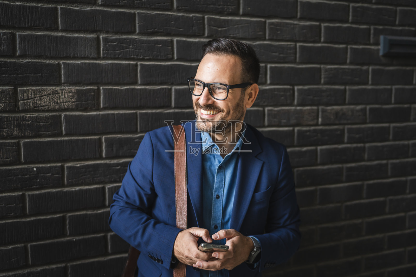 成年商人在黑色墙壁前站着，使用手机。照片摄影图片