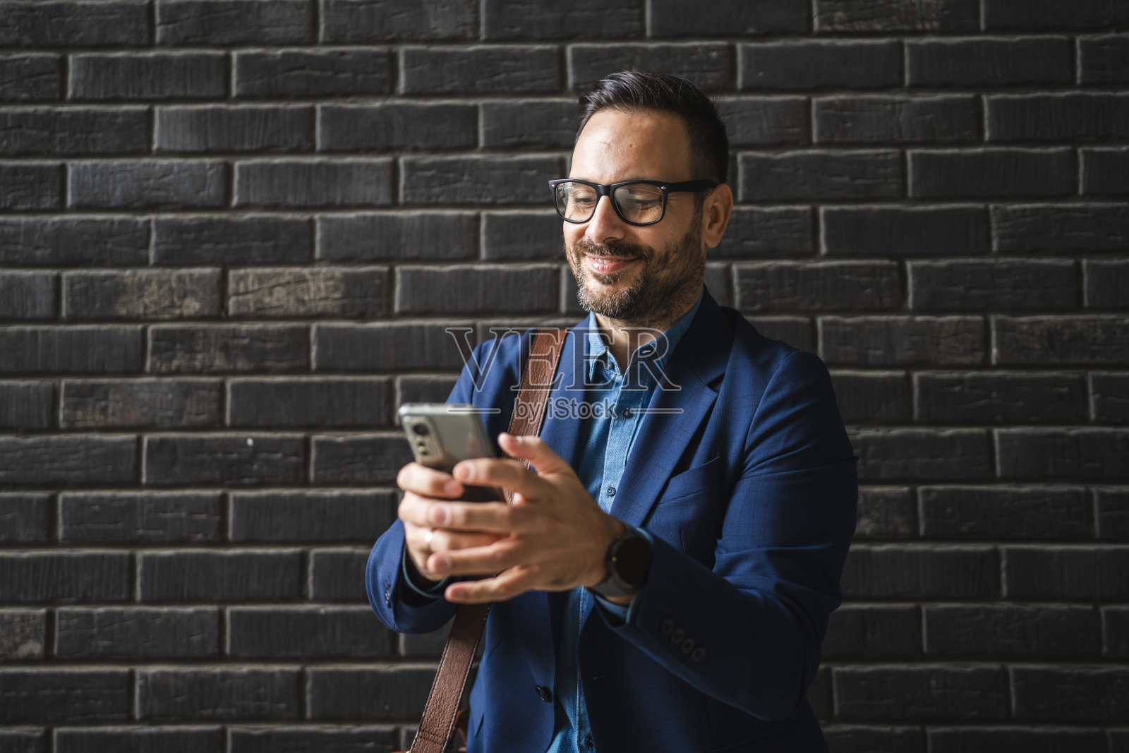 成年商人在黑色墙壁前站着，使用手机。照片摄影图片