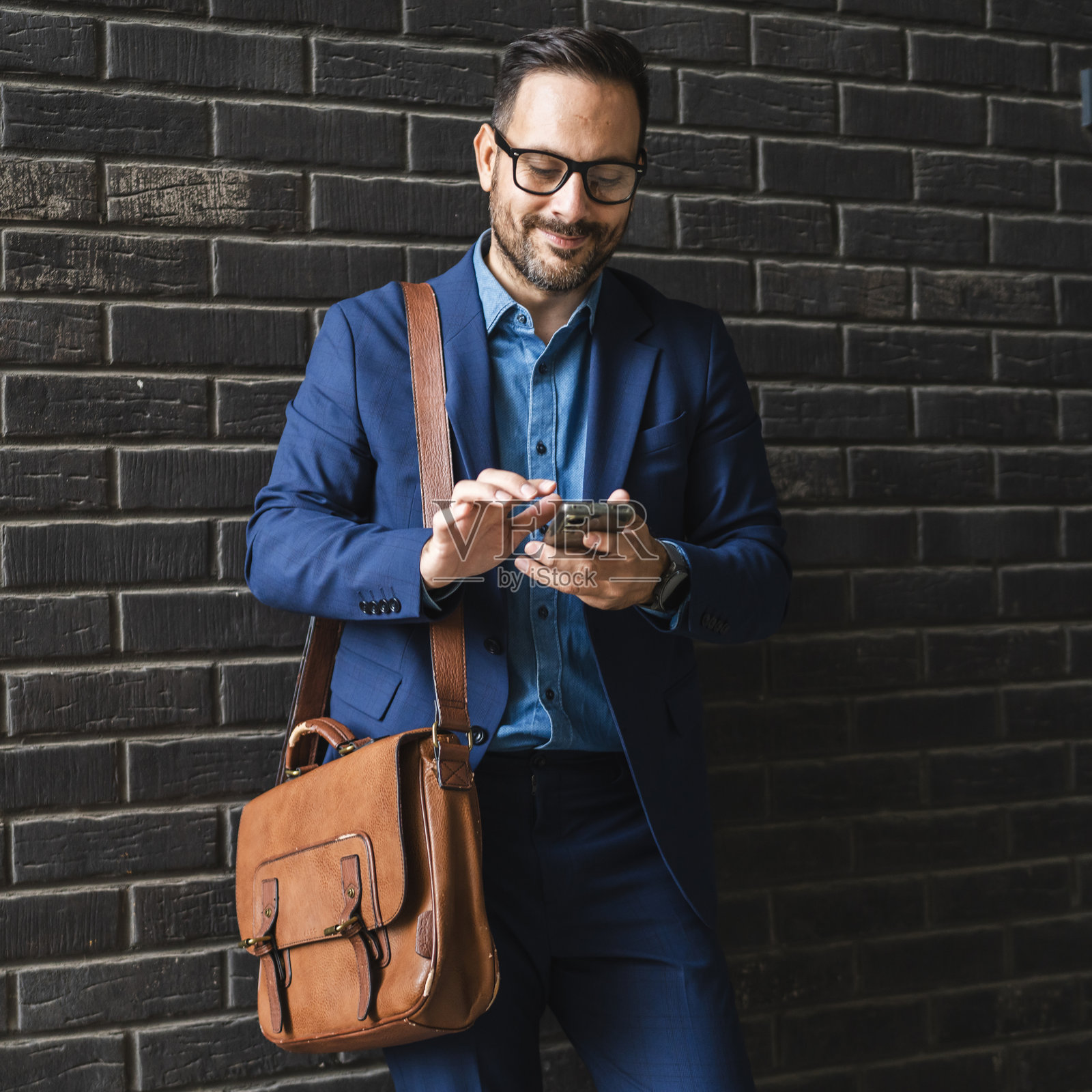 成年商人在黑色墙壁前站着，使用手机。照片摄影图片