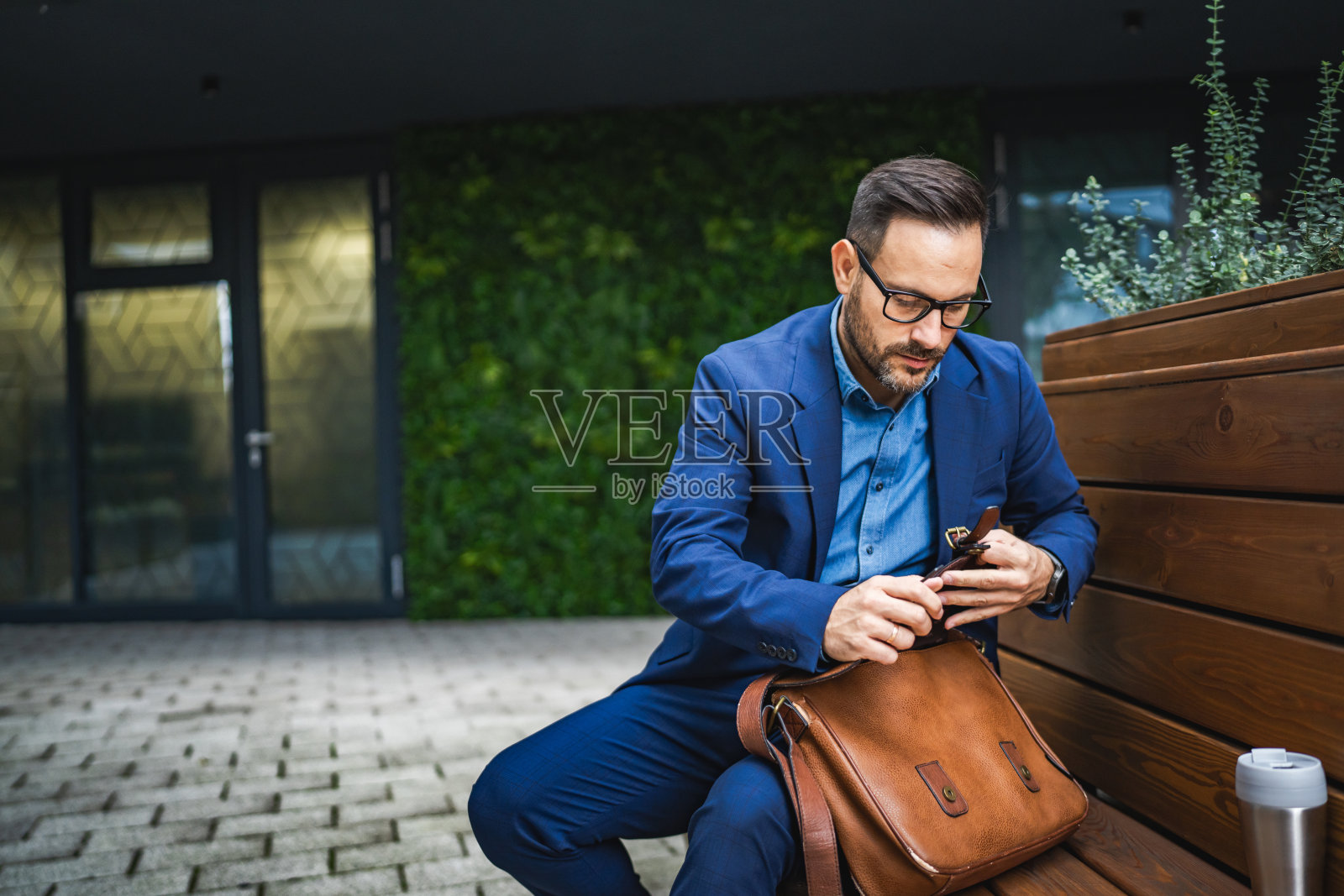 成年男子坐在长椅上准备工作，从公文包中拿出他的笔记本电脑。照片摄影图片