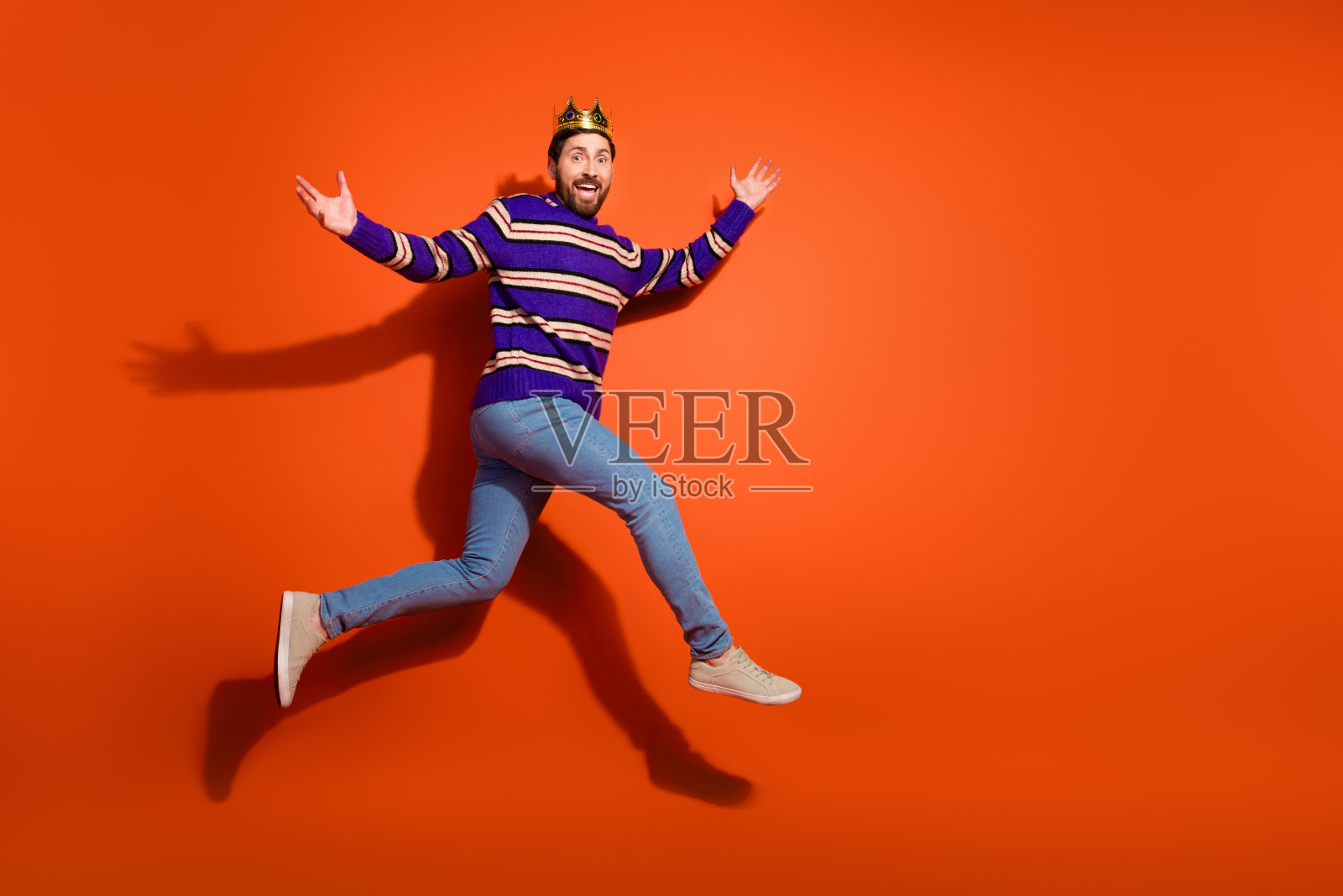 全身照，吸引人的年轻男子兴奋地奔跑，穿着时尚的紫色条纹服装，背景为橙色。照片摄影图片