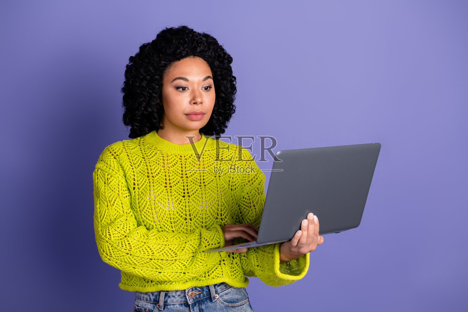 穿着时尚黄色衣服的迷人年轻女性手持笔记本电脑，背景为紫色。照片摄影图片