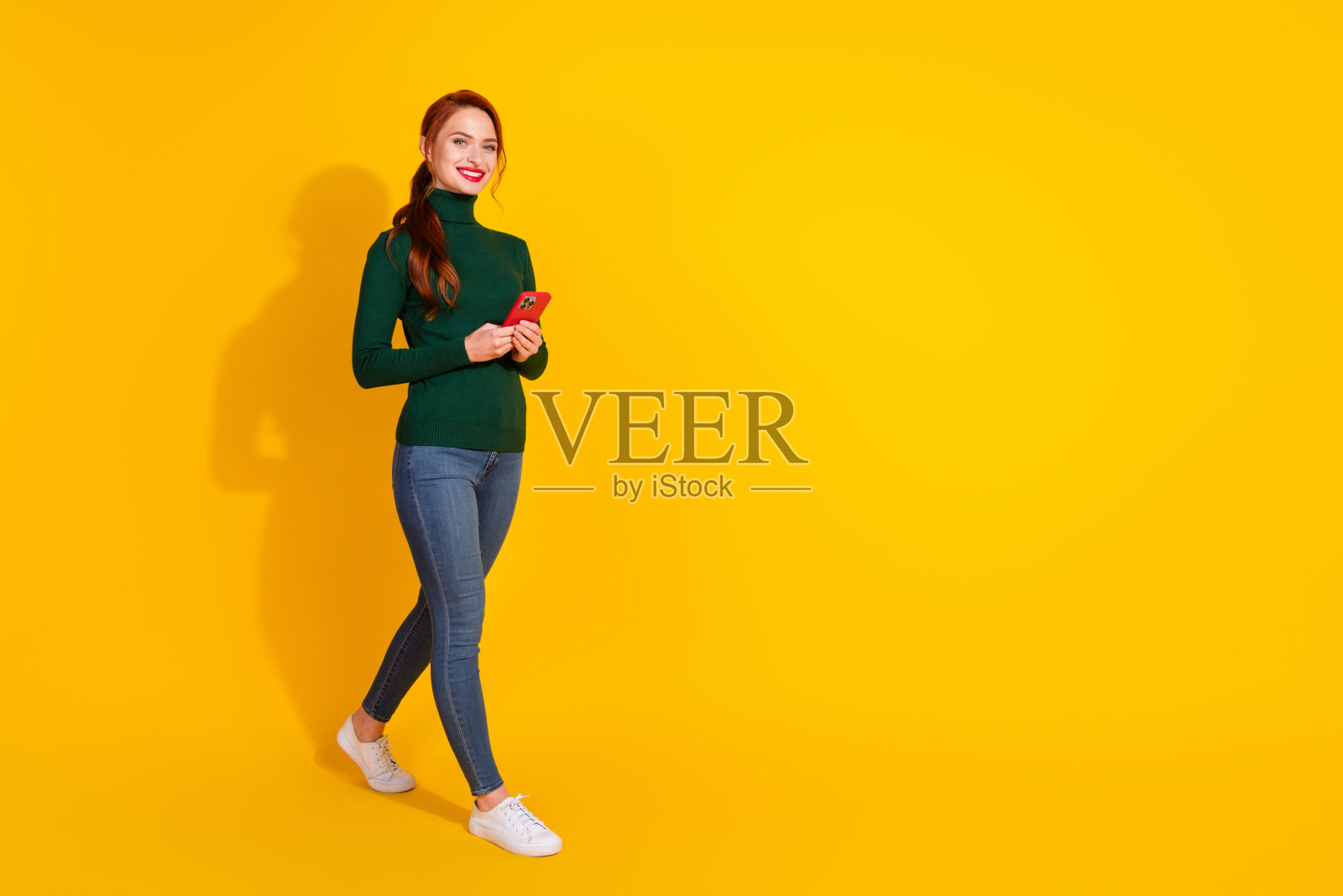 可爱的小女孩穿着绿色毛衣，正在现代设备上打字，背景为空旷的黄色。照片摄影图片