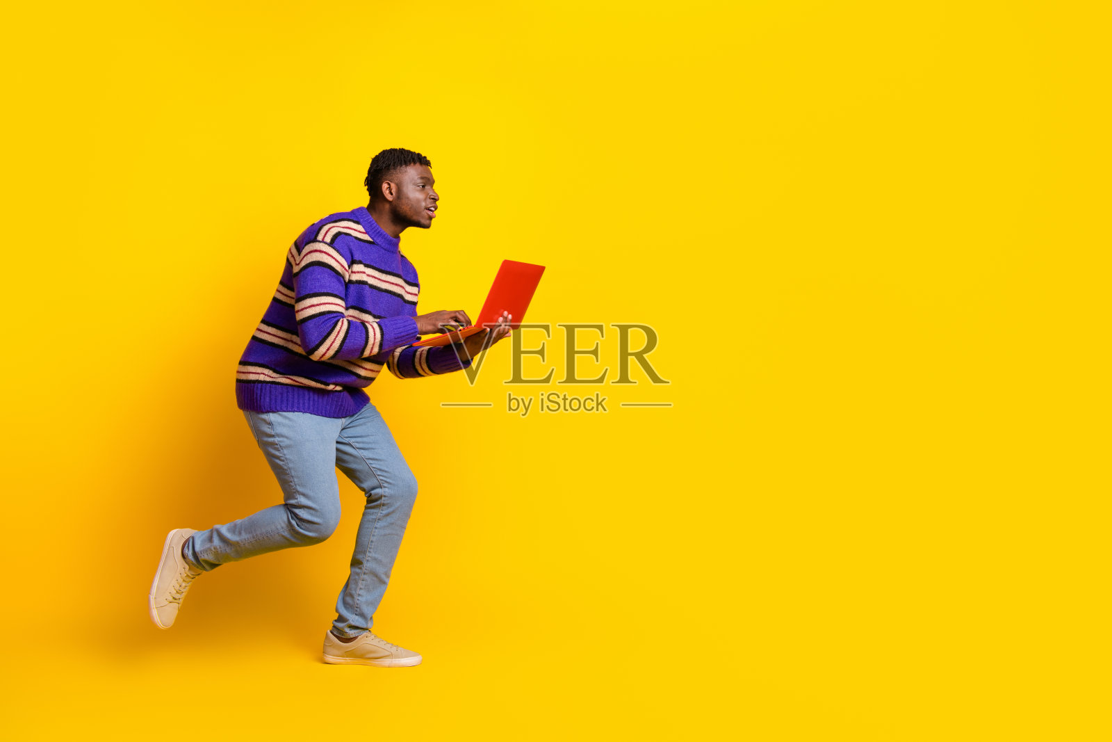 年轻男子在黄色背景下空旷的地方奔跑，手中拿着笔记本电脑的全身照片照片摄影图片