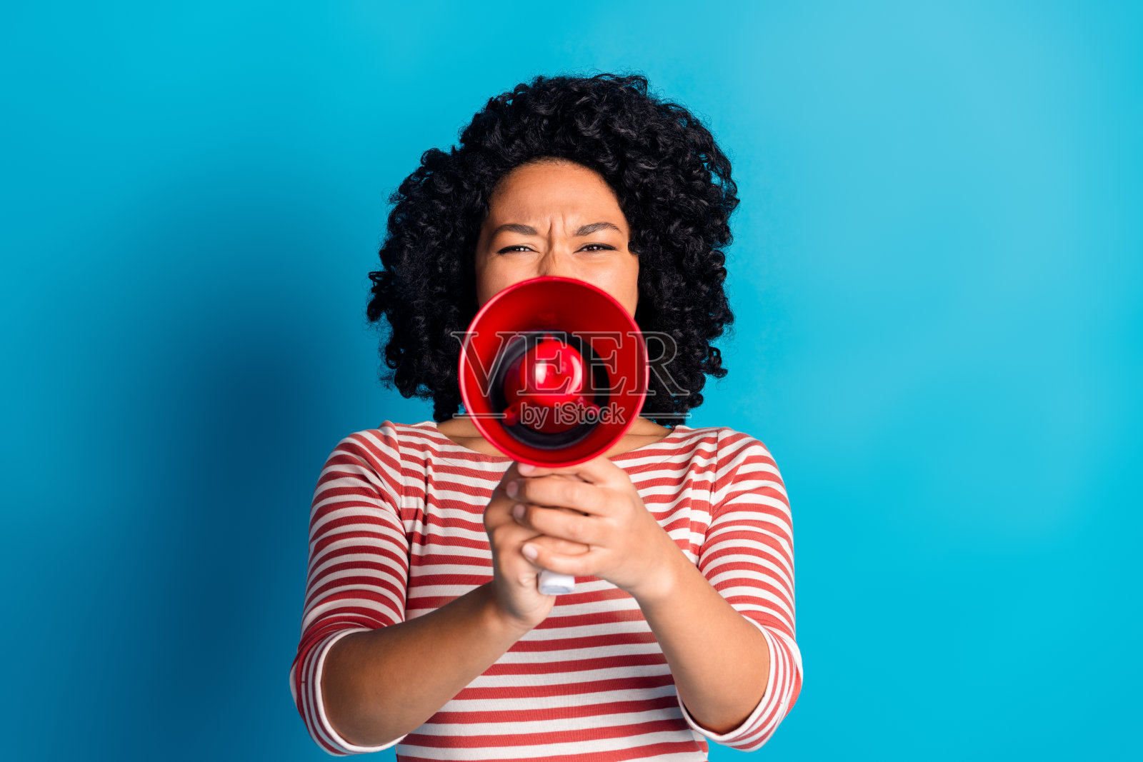 穿着时尚条纹衣服的迷人女孩，手持扩音器在蓝色背景下宣布消息。照片摄影图片